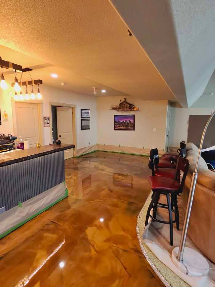 A room with a metallic gold epoxy floor, a bar, and bar stools.
