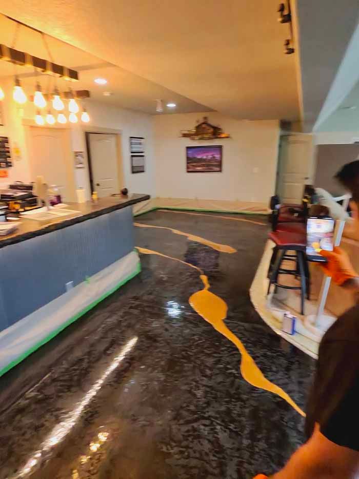 Person filming epoxy flooring with yellow accent on a partially finished basement floor.