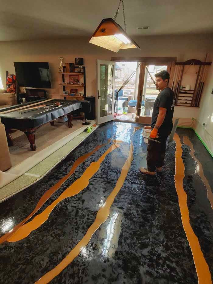 Man applying epoxy to a floor, gold streaks on black, pool table and open door in background.
