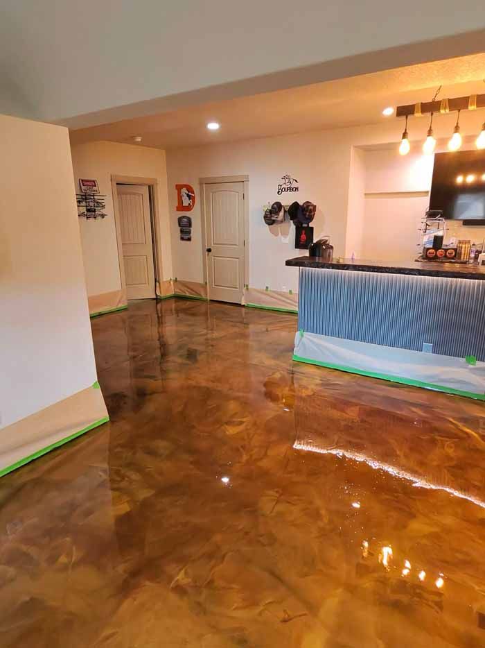Metallic epoxy flooring in a room, with doors and a bar. Green tape is along the edges.
