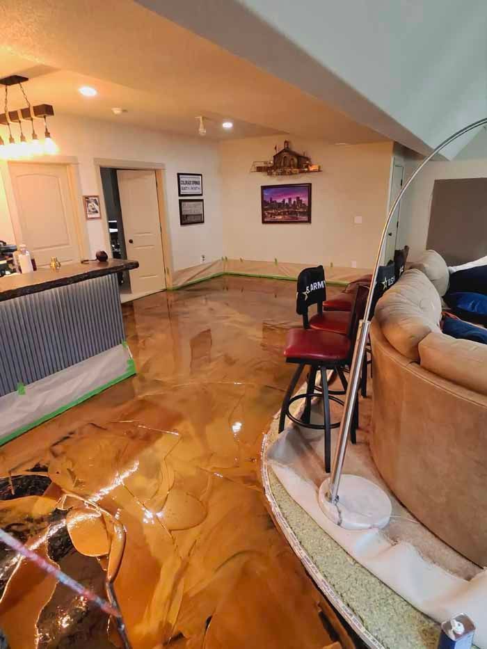 A room with a gold epoxy floor, bar stools, and a boat-shaped sofa.