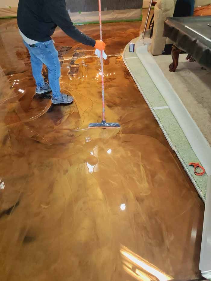 Person applying epoxy to a metallic brown floor with a squeegee.