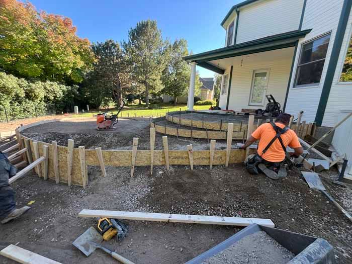 Construction workers building a curved concrete patio with steps near a white house.