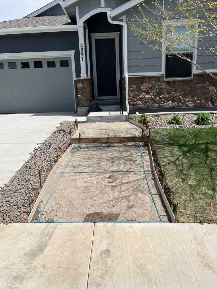 Concrete forms for a front walkway under construction, leading to a house with a gray exterior.