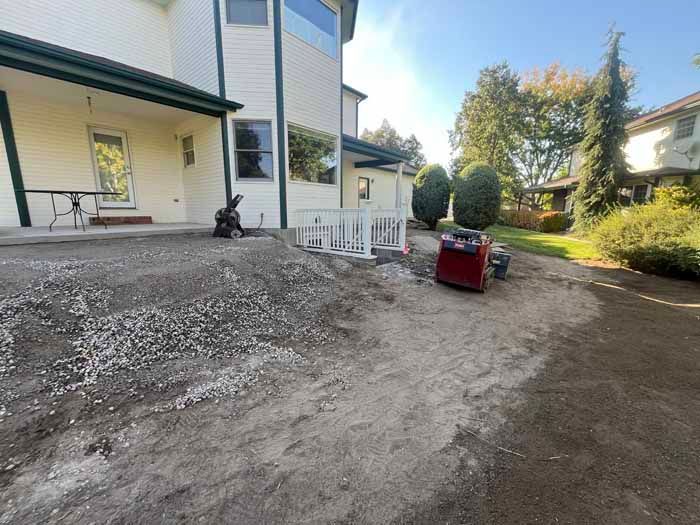 Construction site next to a house with gravel, soil, and machinery. Sunlight.