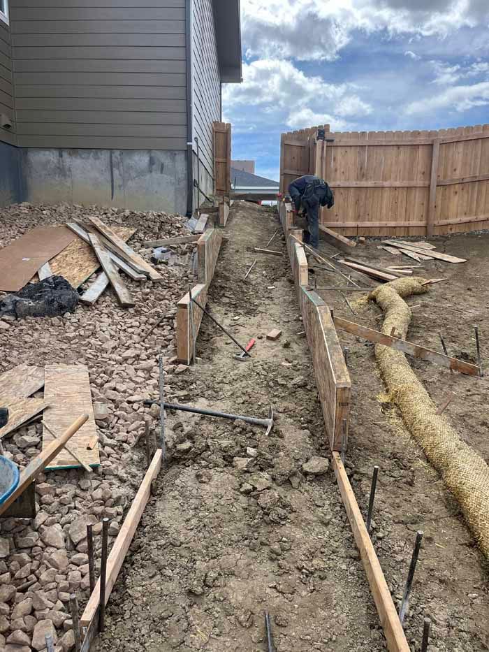 Construction of a concrete walkway on a hillside. Wooden forms, rebar, and a person working are visible.