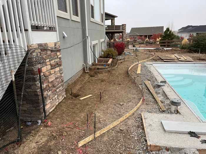 Construction site next to a house and pool, with wooden forms outlining a curved pathway.