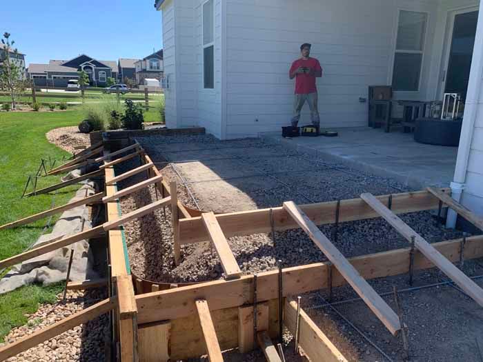 Construction site: wooden forms for a retaining wall and patio. A person stands nearby, observing.
