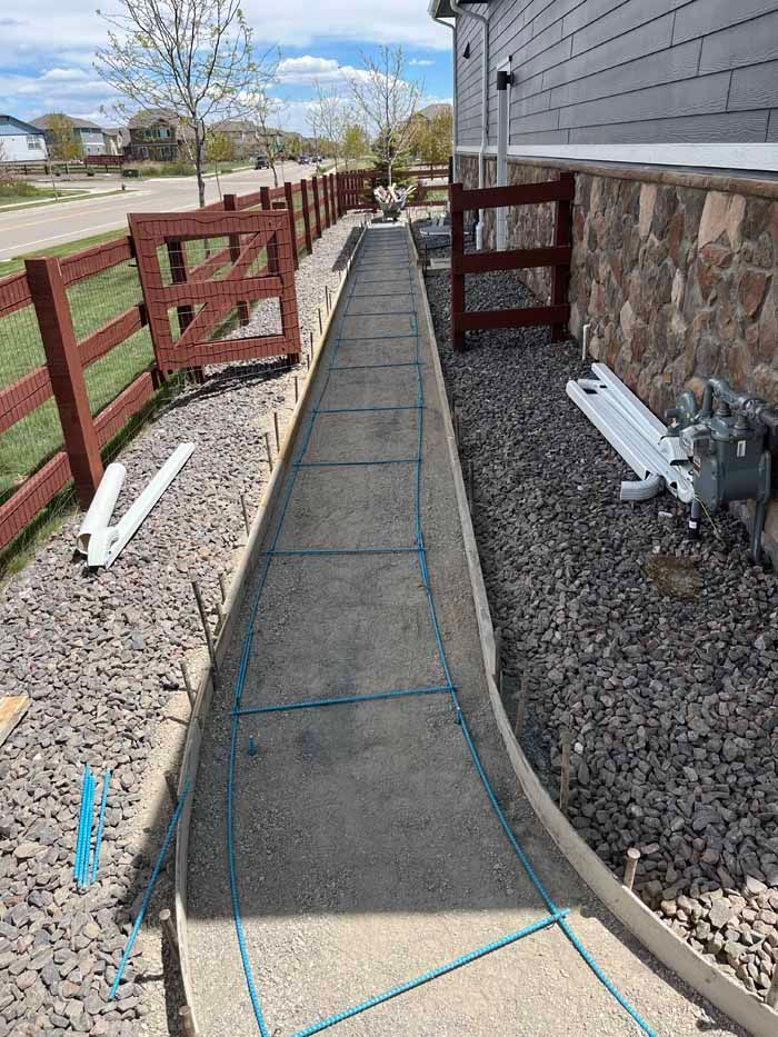 Concrete walkway being constructed beside a house with a red fence and gravel borders.