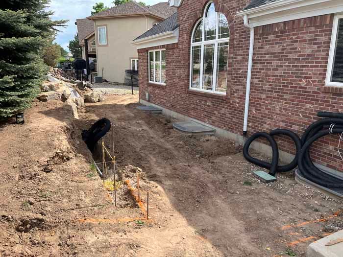 A trench dug along a brick house; black pipes and landscaping work underway.