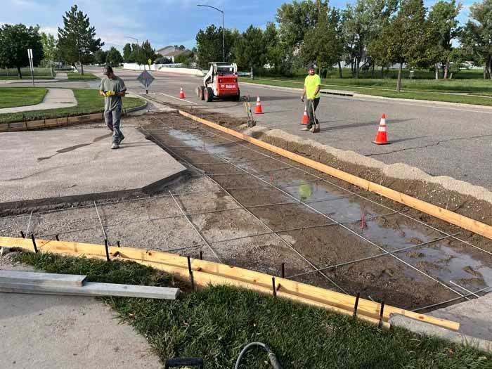 Road construction site: Workers, bobcat, concrete forms, and fresh concrete on a street.