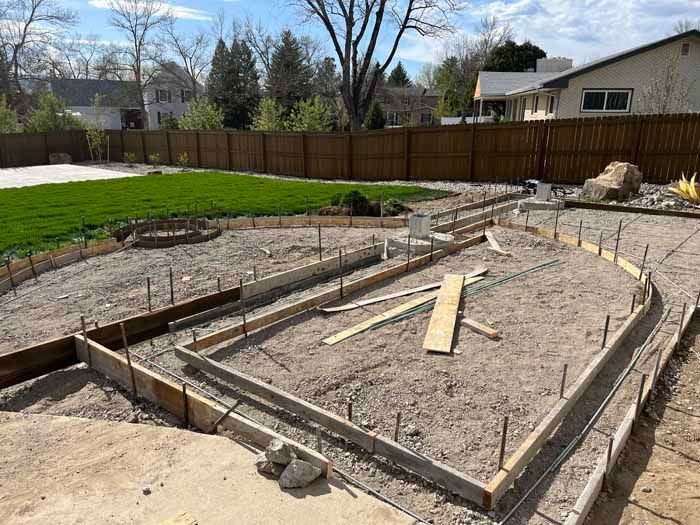 Construction of concrete forms in a backyard, with gravel base and wooden frames.