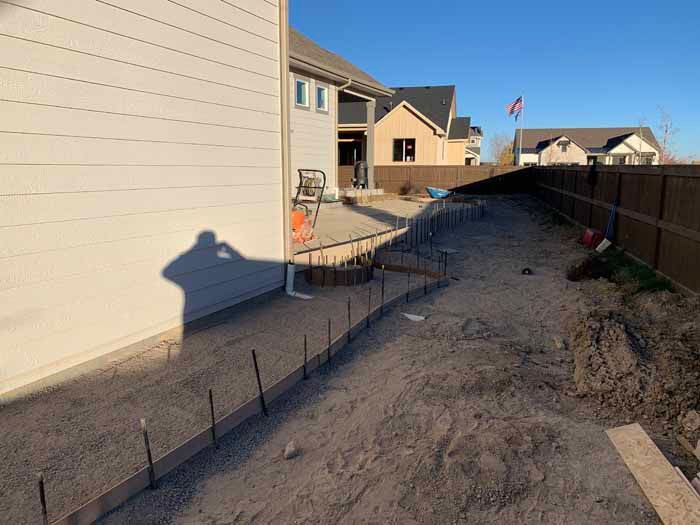 Construction site: Concrete forms outline a pathway in a yard, next to a house with a shadow cast.