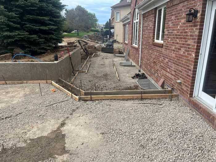 Construction site: gravel and concrete forms next to a brick building.