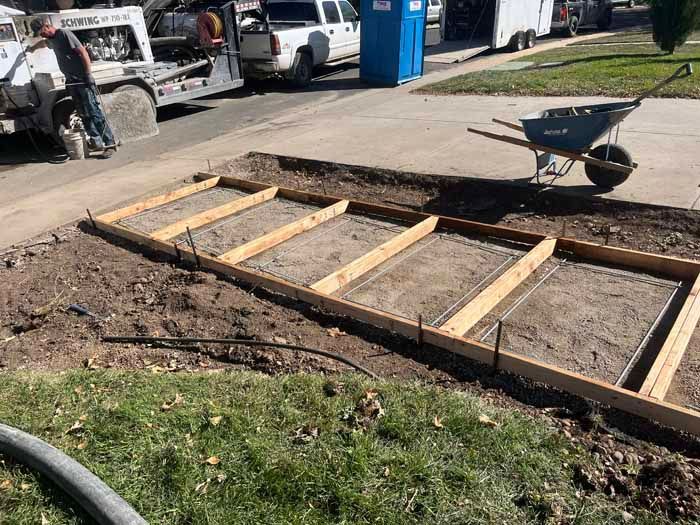 Construction site: Forms for a concrete driveway section, rebar grids, a worker, wheelbarrow, and concrete truck.
