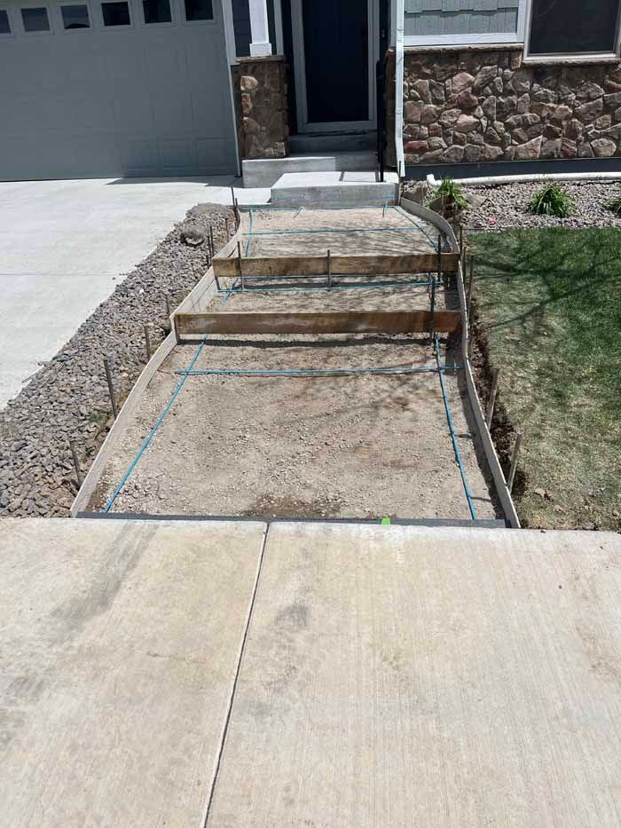 Construction of concrete steps leading to a house entrance. The area is prepped with forms and rebar.