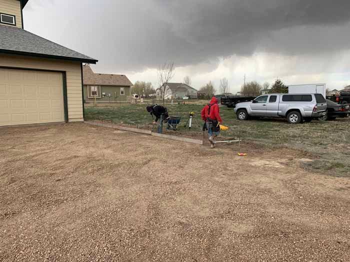 Person in red jacket walking toward a dog on a cloudy day next to a house and driveway.