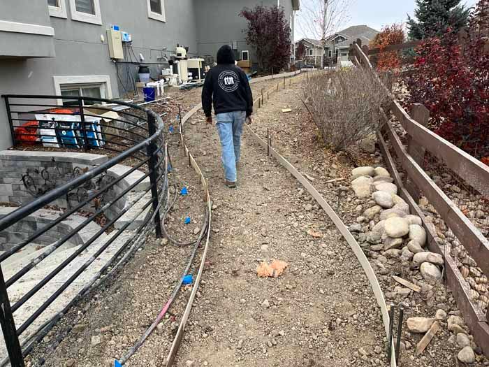 Person walking on a dirt path with concrete edging, alongside a fence and a retaining wall.