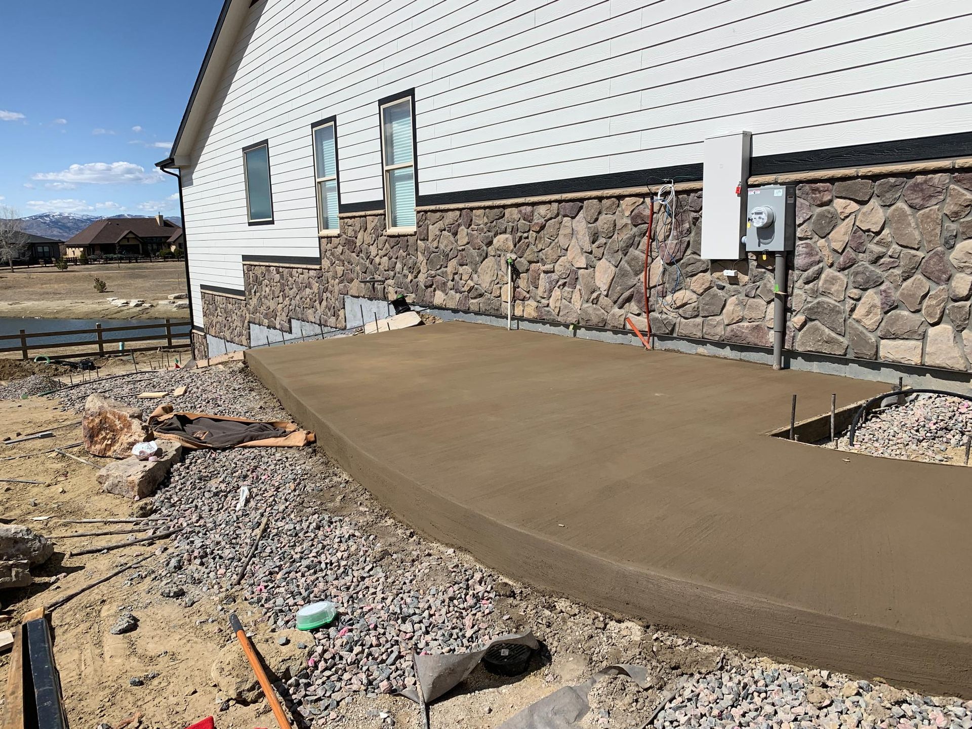 Newly poured concrete patio next to a house with white siding and stone veneer.