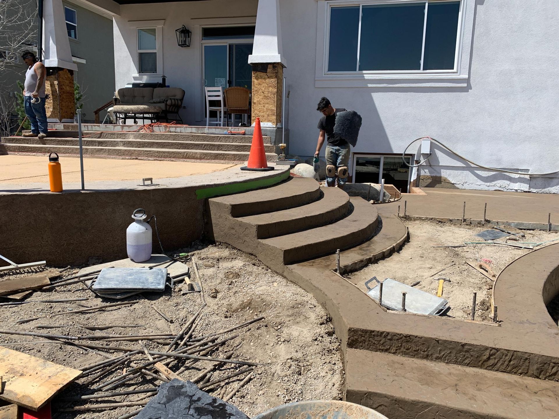 Construction workers pouring concrete for new curved steps at a house entrance.