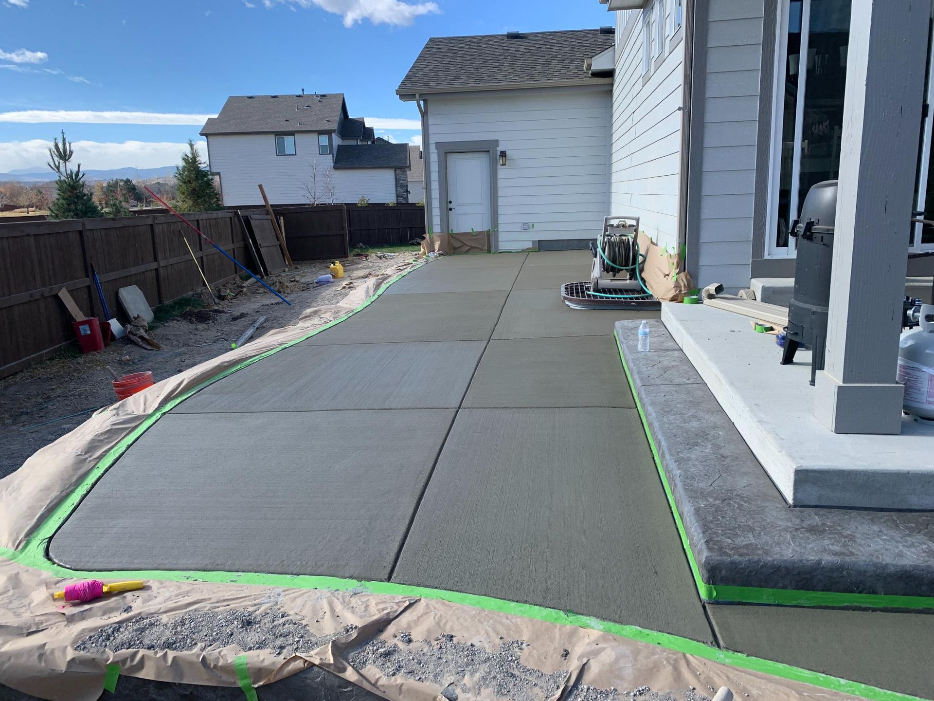 New concrete patio with expansion joints, next to a house and fenced yard.