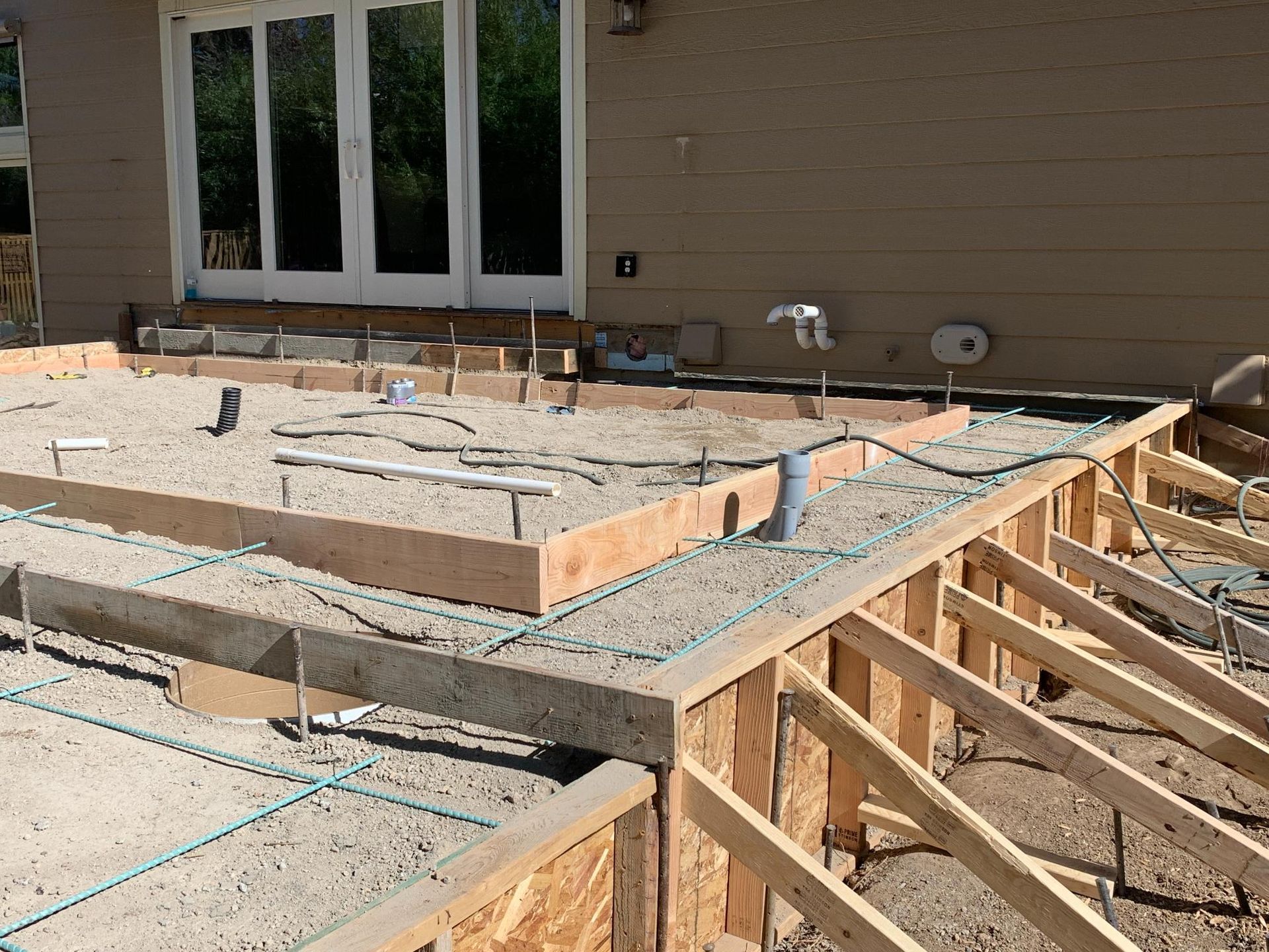 Construction site with wooden forms and rebar, preparing for concrete patio installation.