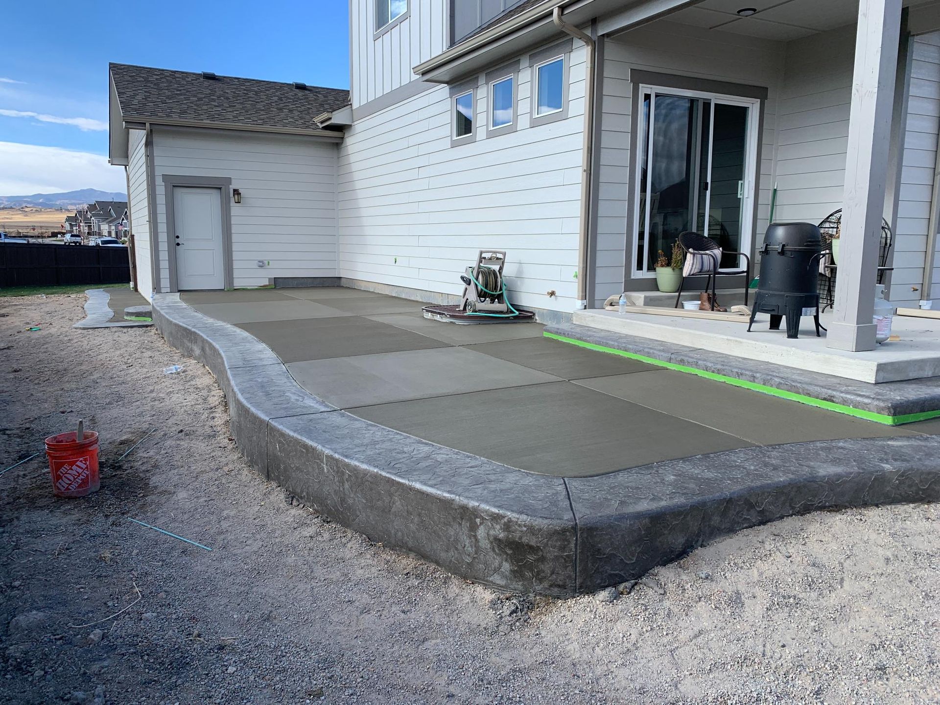 Newly poured concrete patio next to a house with a rounded border and gravel.