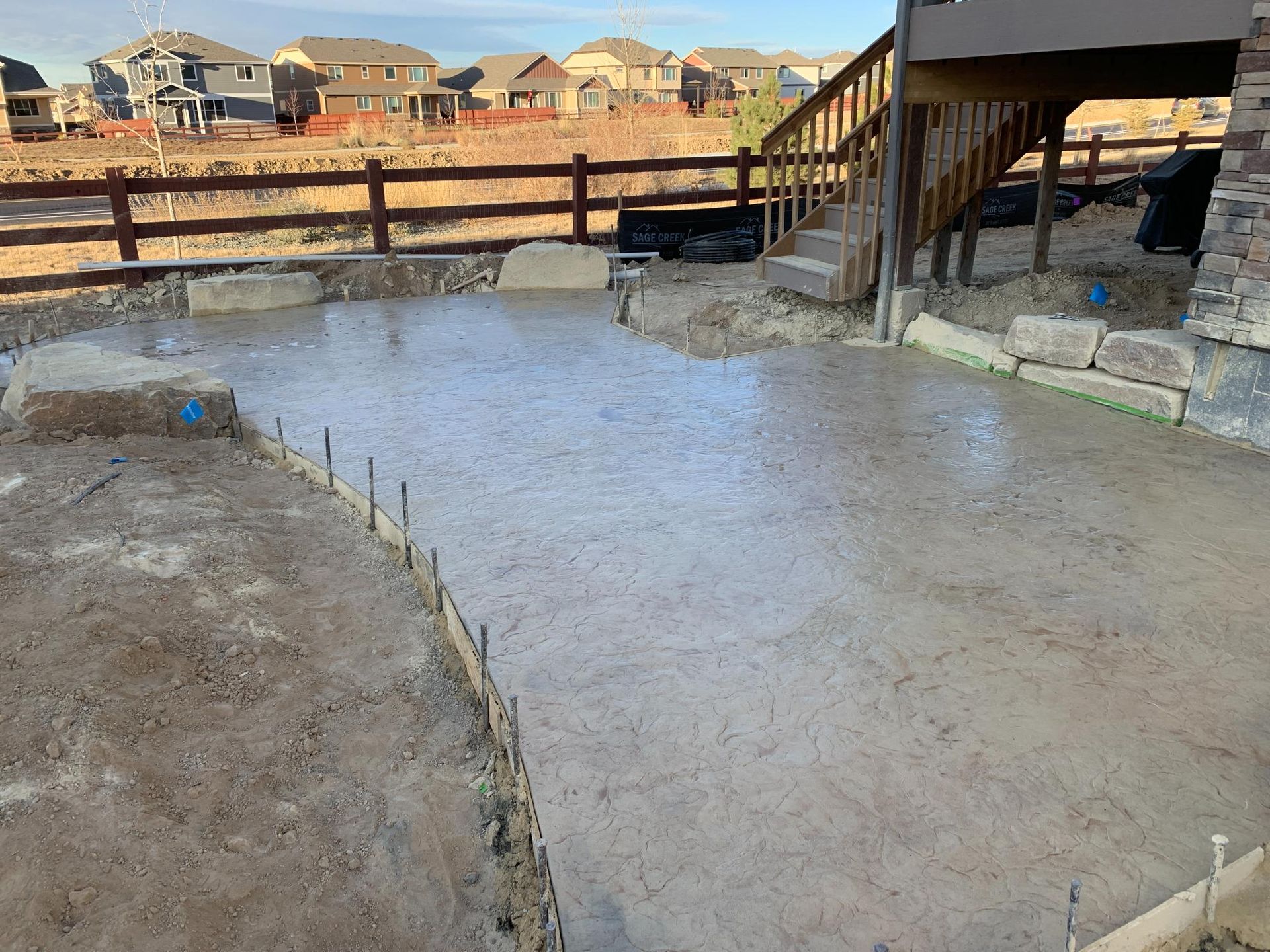 Freshly poured concrete patio with wooden deck and fence in background.