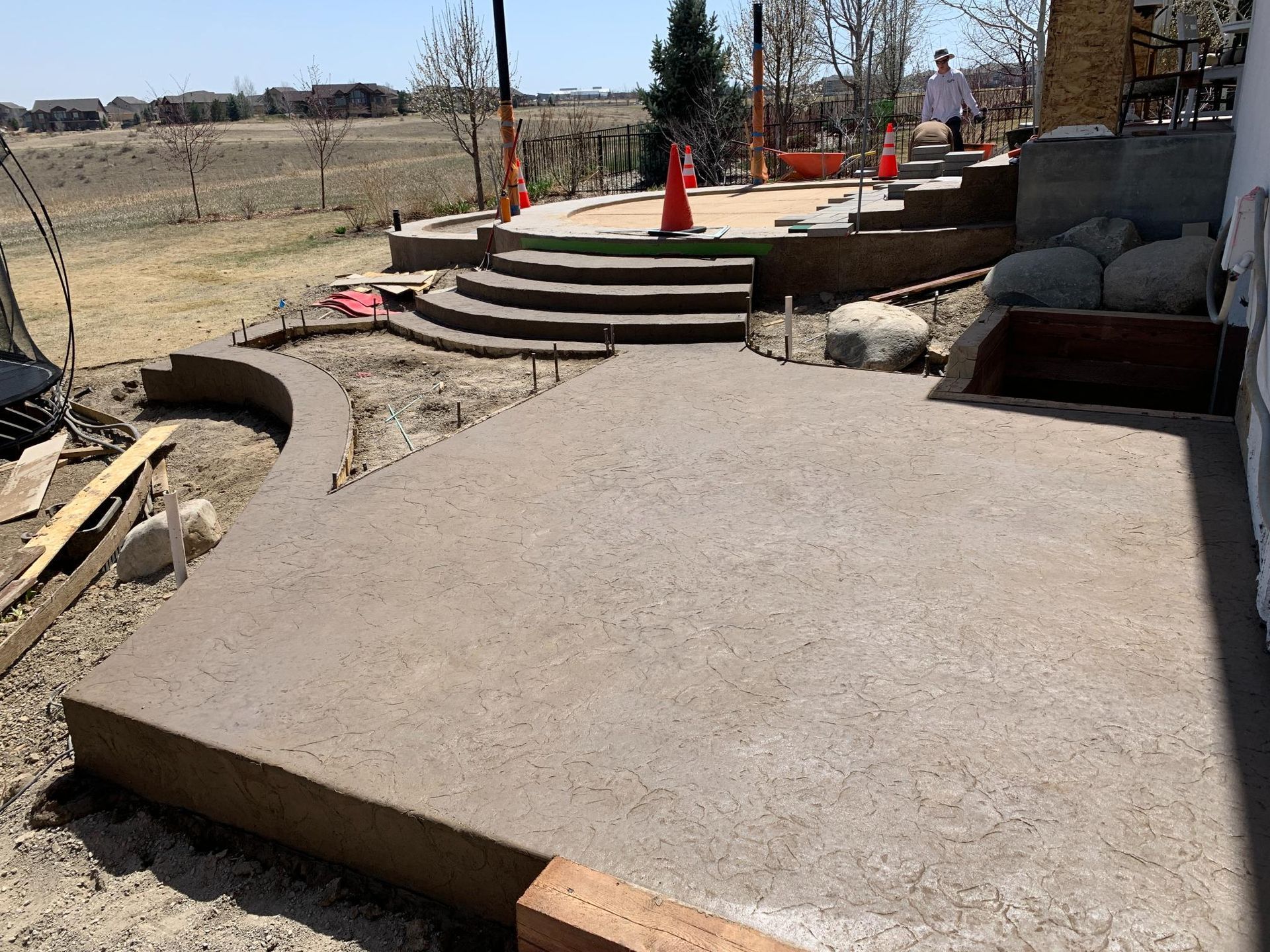 Newly poured concrete patio and steps being built outdoors. Person visible in the background.