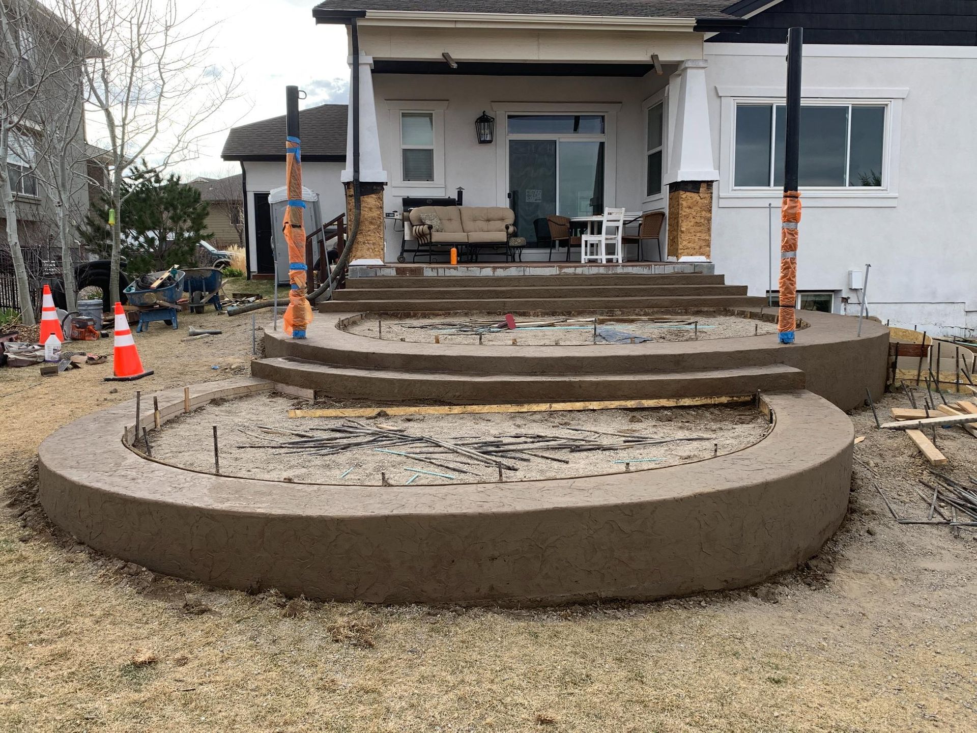 Concrete patio construction with curved steps and retaining walls, near a house.