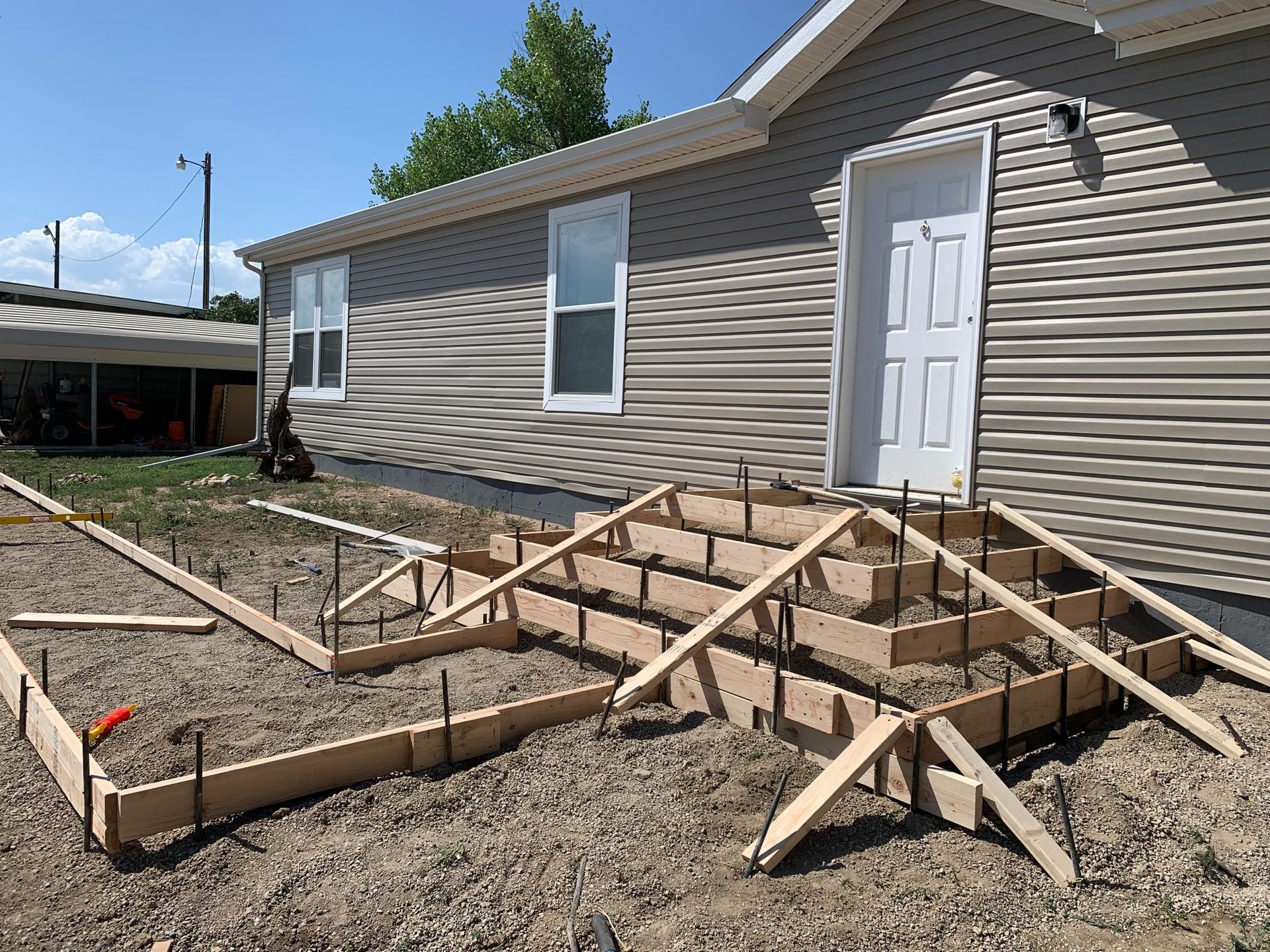 Concrete steps under construction in front of a house. Forms, rebar, and support beams visible.