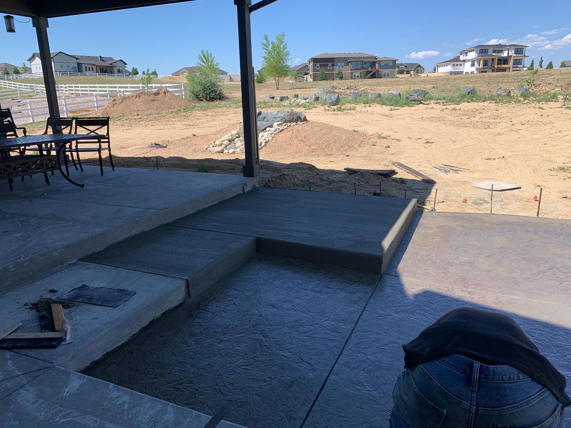 Newly poured concrete patio with steps under a pergola, dirt in background.