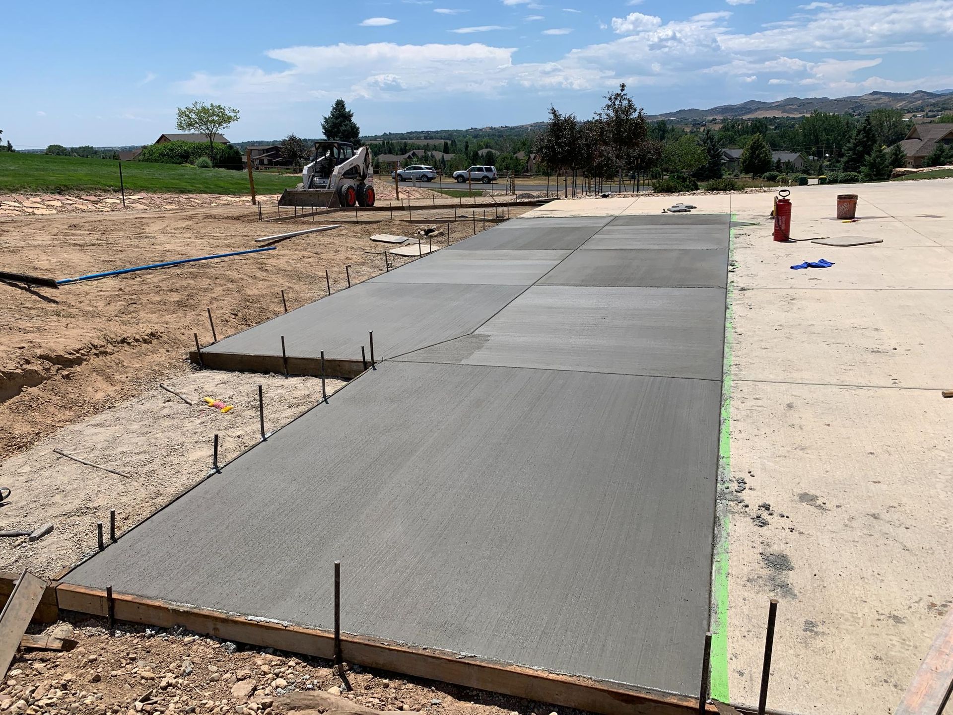 Newly poured concrete sidewalk with wooden forms and rebar at a construction site on a sunny day.
