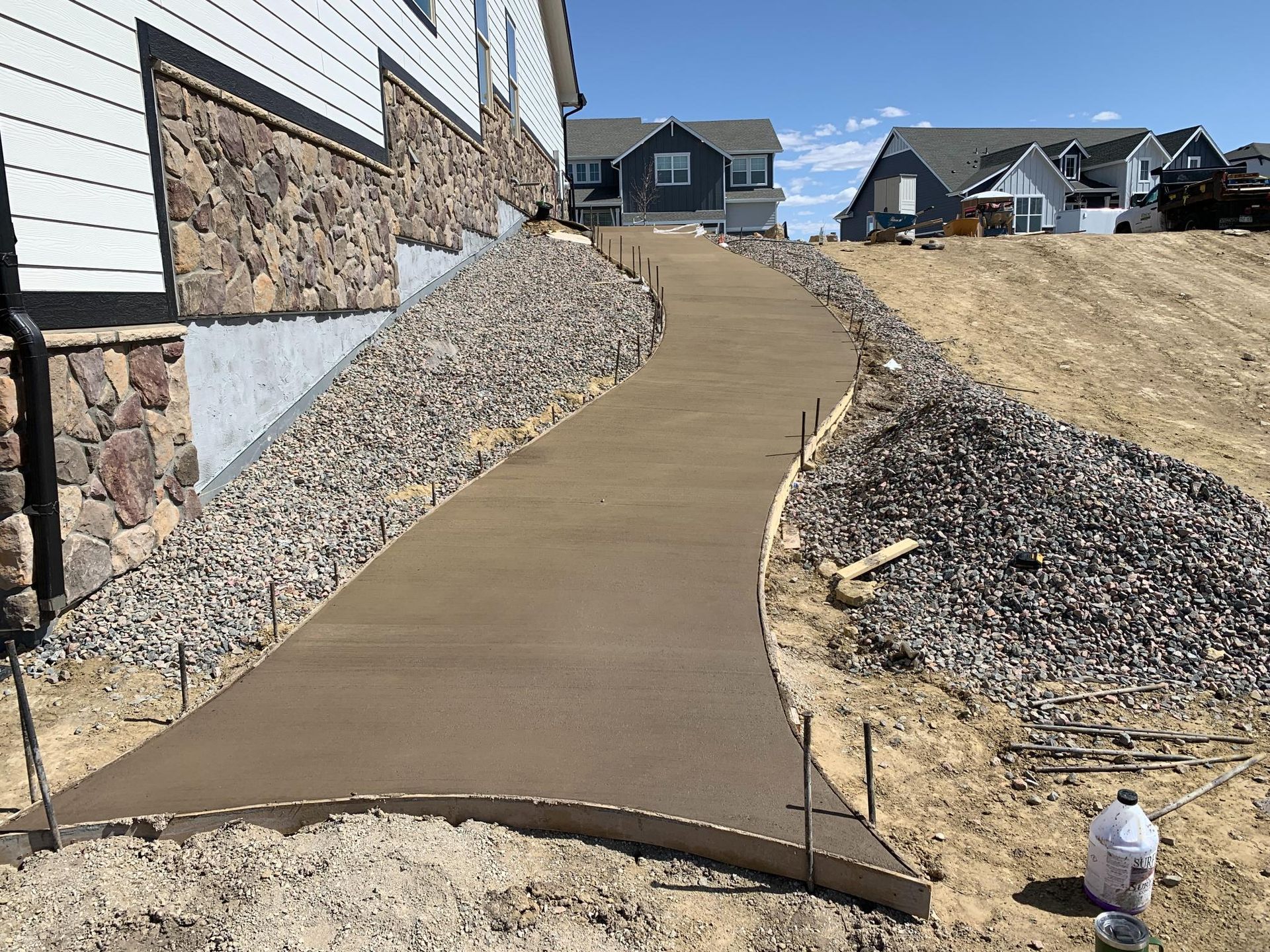 Newly poured concrete walkway next to a building, sloping uphill with rock retaining walls.