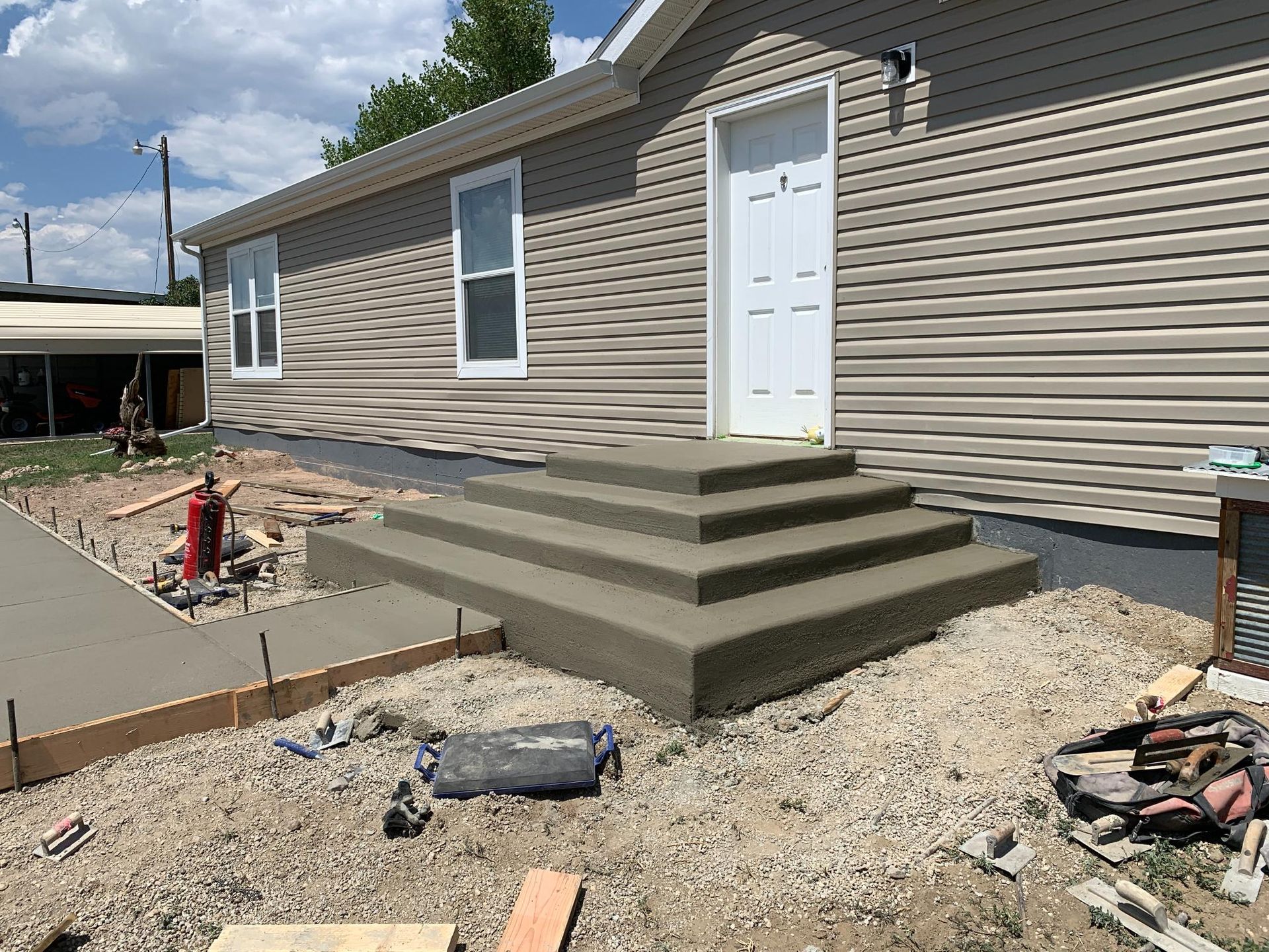 New concrete steps leading to a white door of a tan sided house; new walkway on the left.