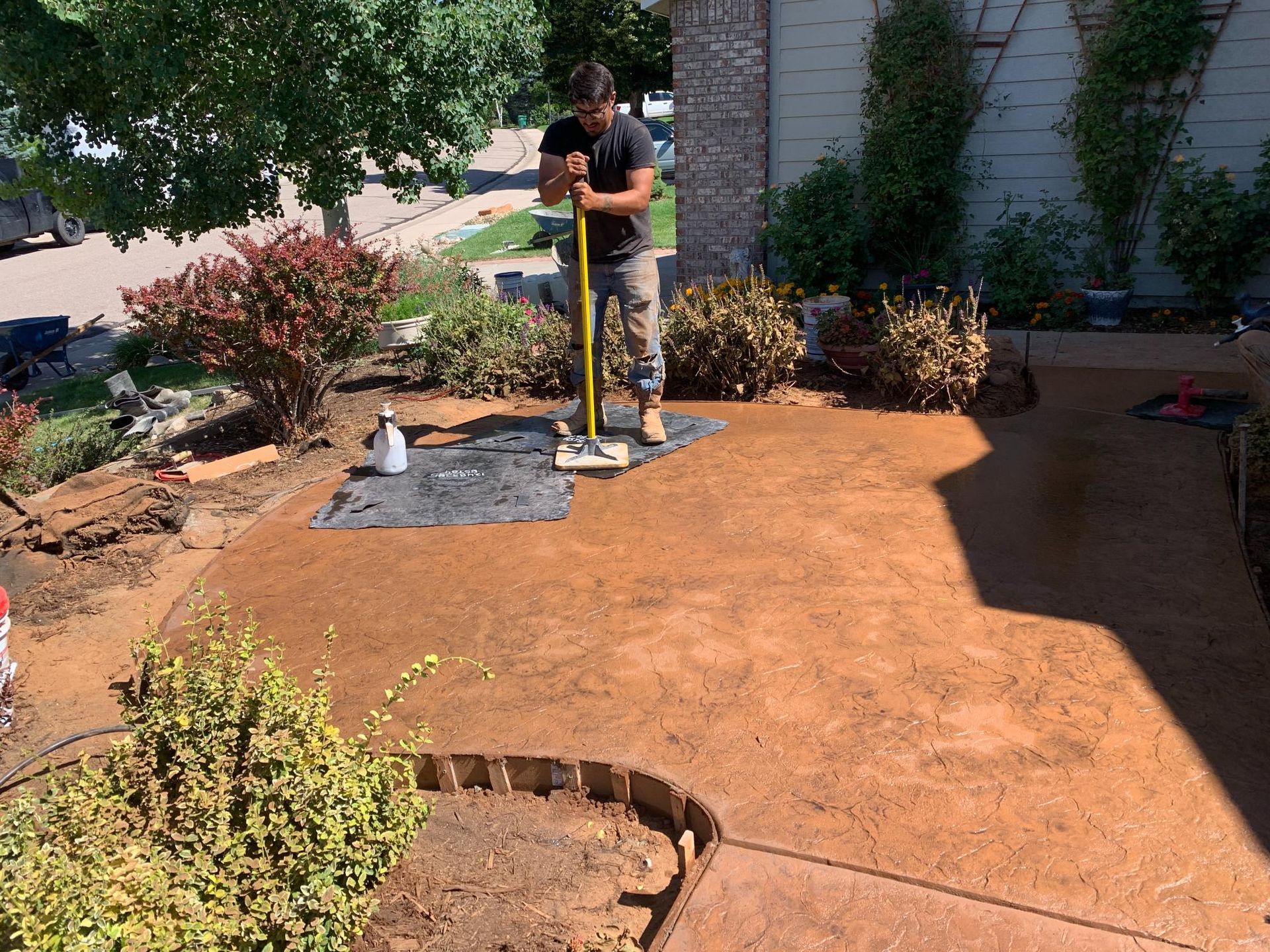 Man compacting ground with a tamper tool in a front yard landscaping project.
