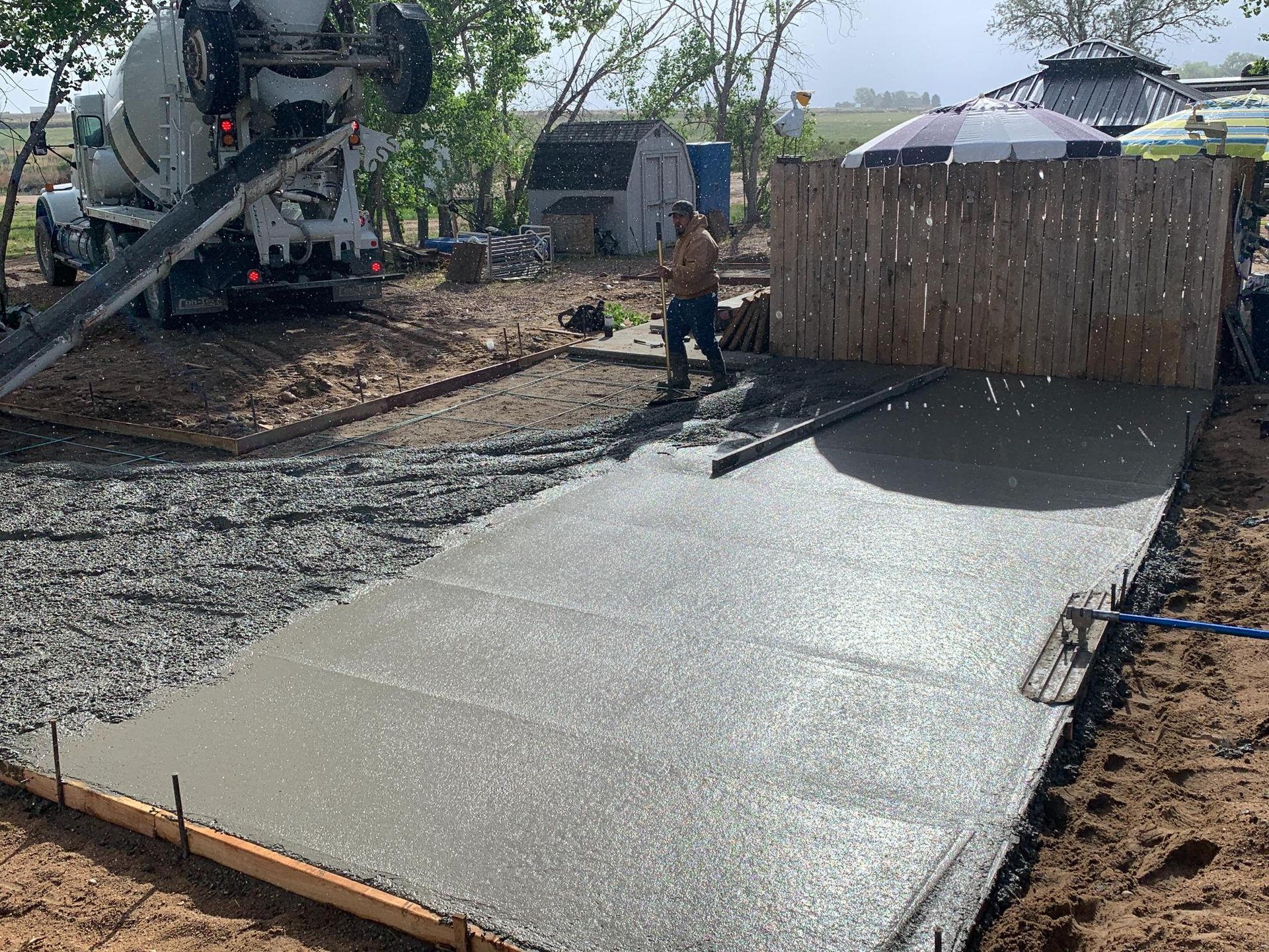 Concrete being poured from a truck onto a framed area, leveled by a worker. Outdoors.