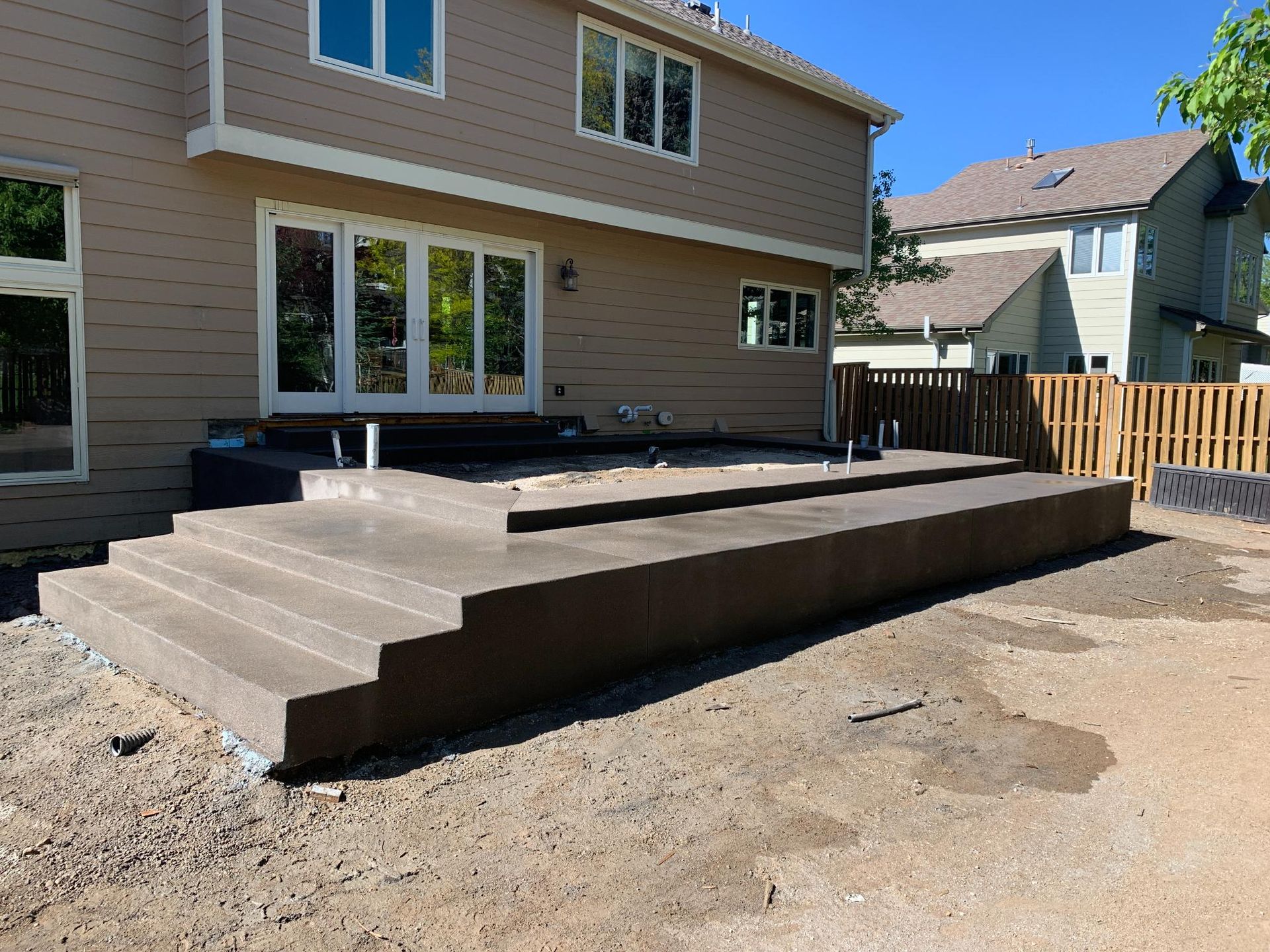 Concrete patio with steps leading to a house with large windows.