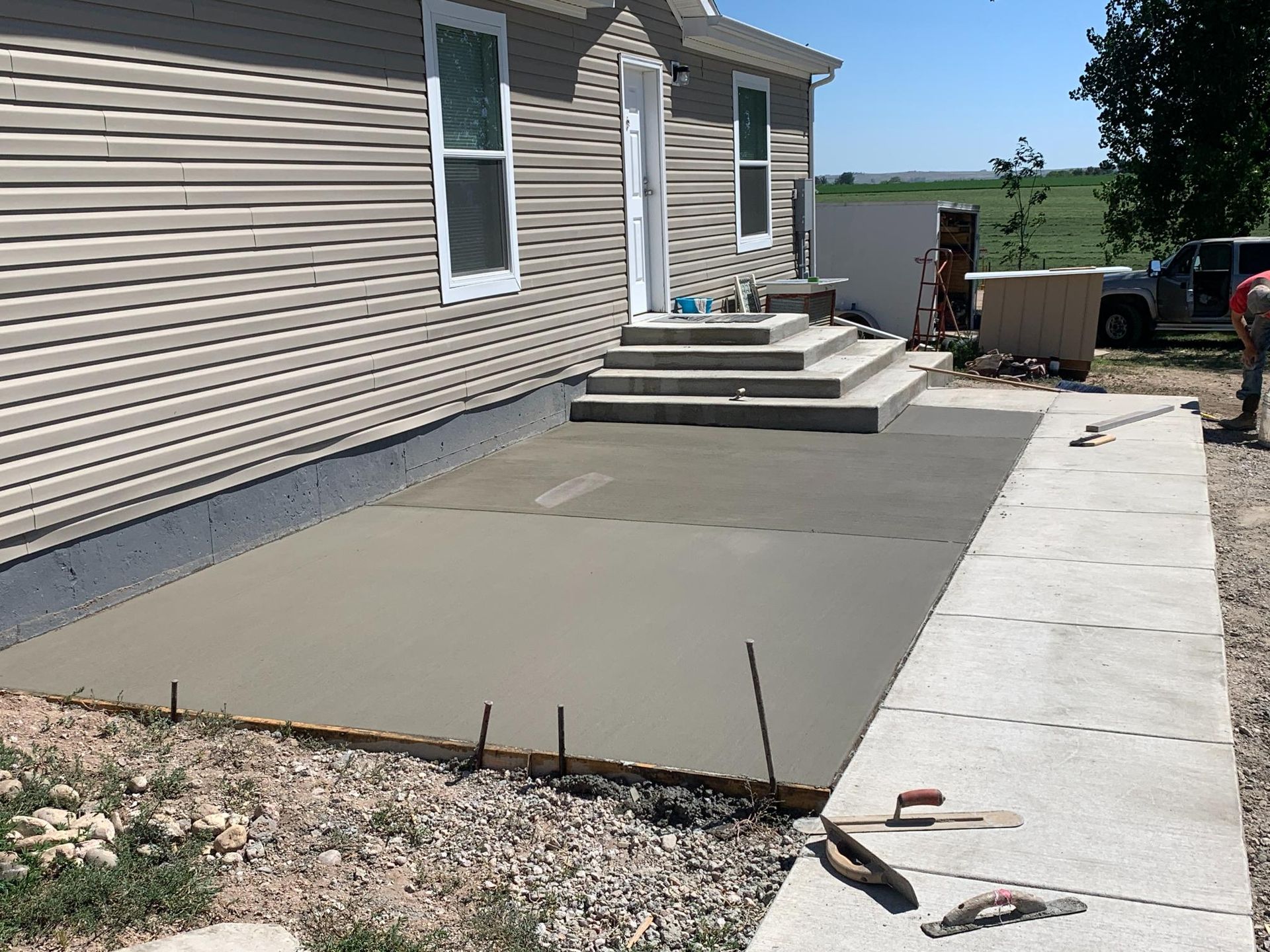 Freshly poured concrete patio beside a house. Rebar and tools present.