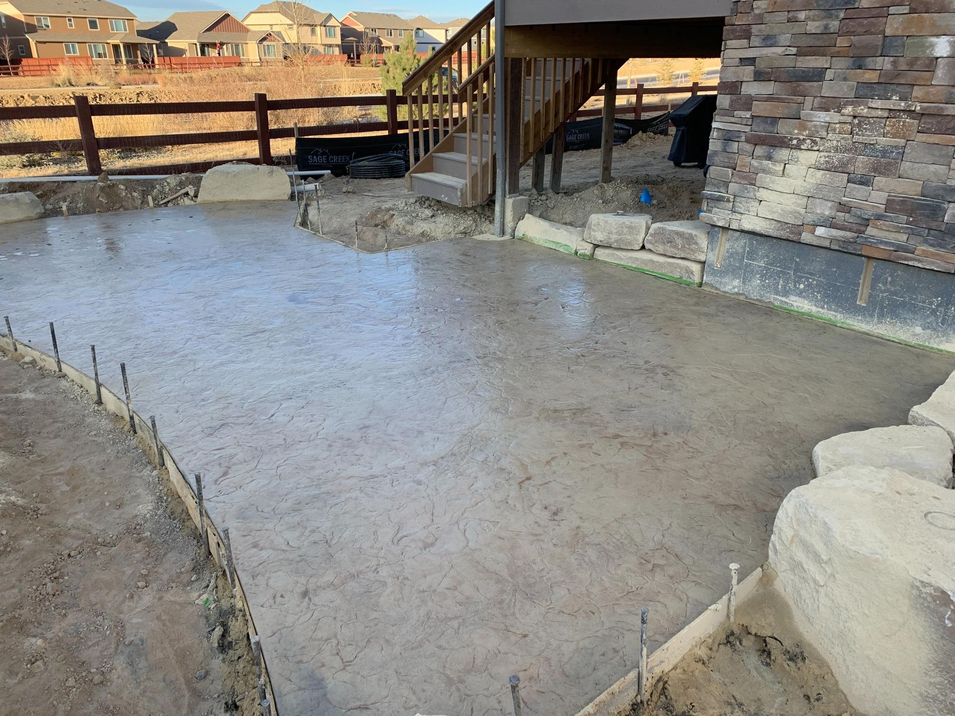 Newly poured concrete patio next to a house with a wooden deck.