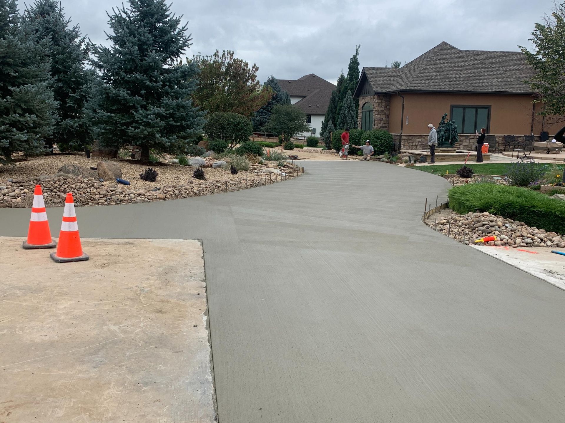 Freshly poured concrete driveway with safety cones, trees, and house in the background.