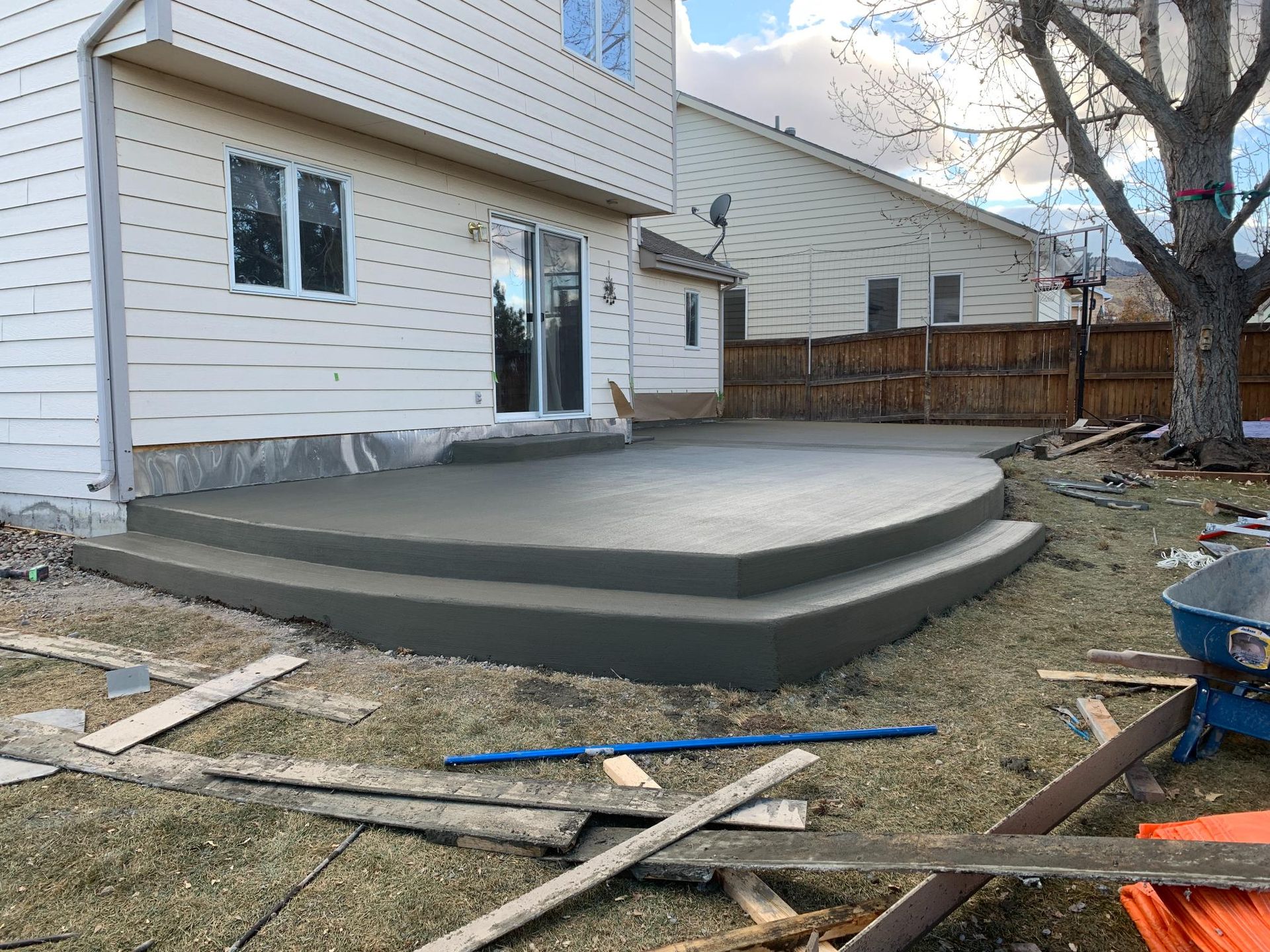 Newly poured concrete patio with steps in a backyard setting.