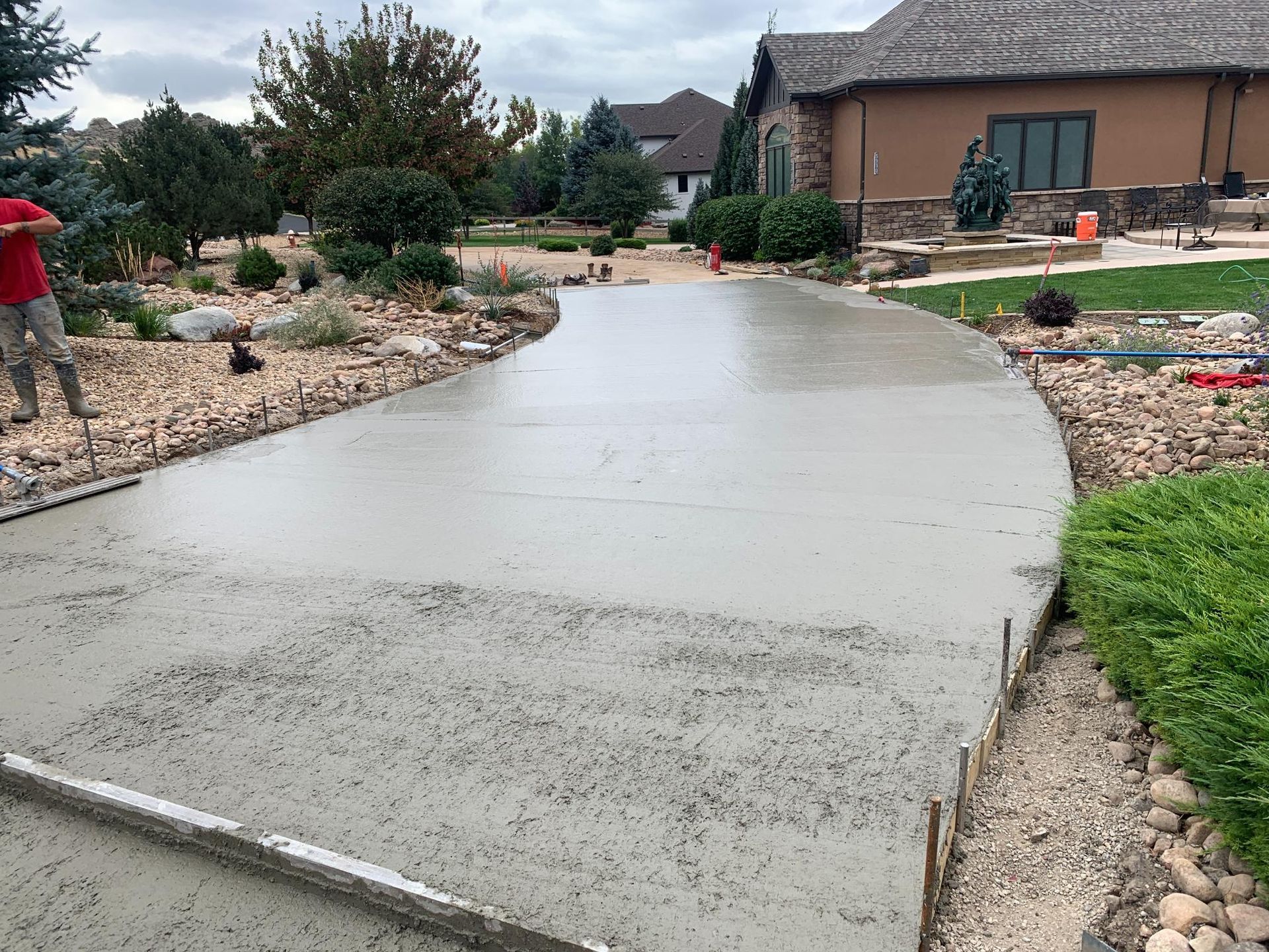 Freshly poured concrete driveway curving toward a house; a person is visible on the left.