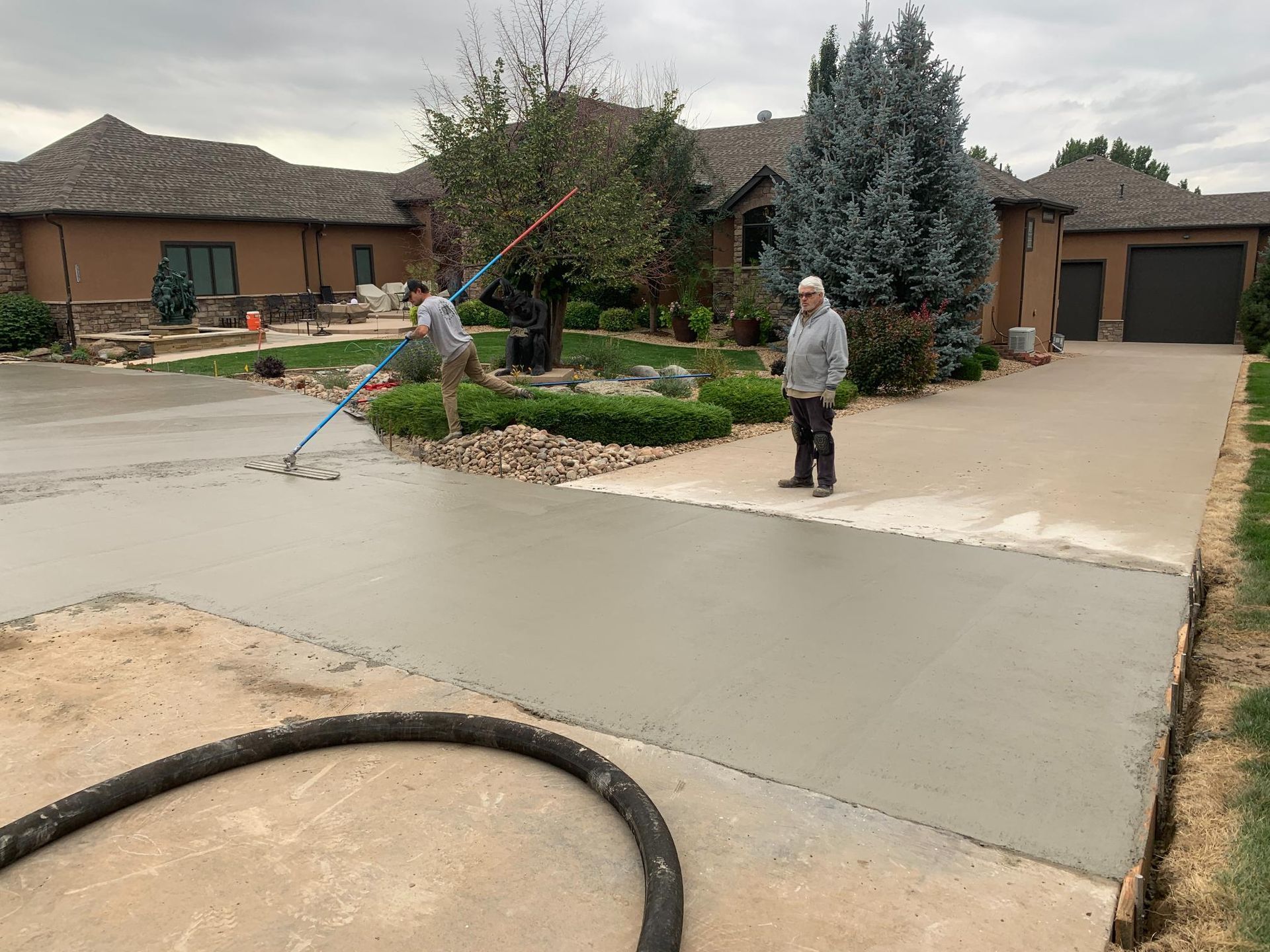 Two people pouring fresh concrete driveway in front of a house.