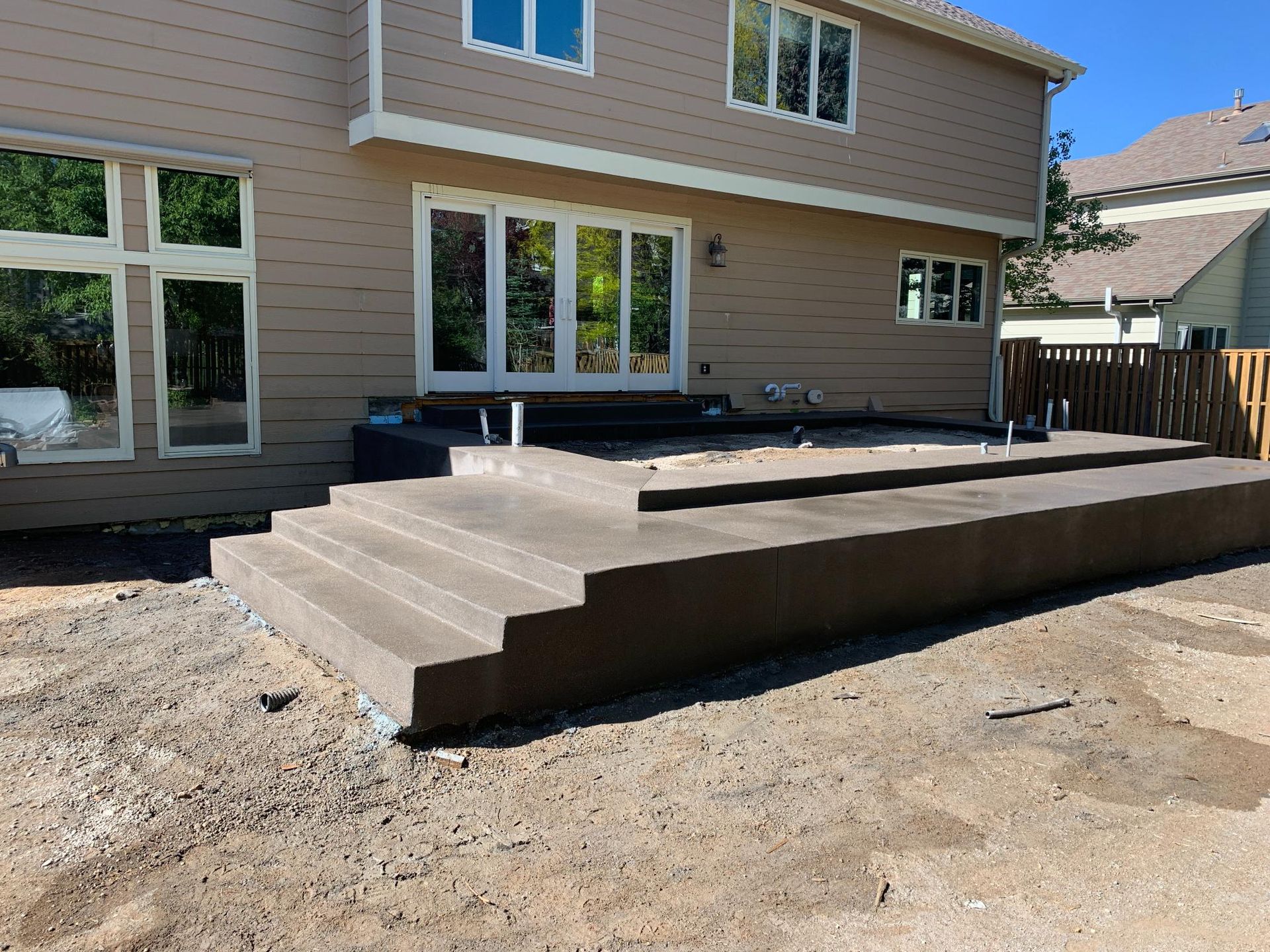 Concrete steps leading up to a concrete patio outside a light brown house with large windows.