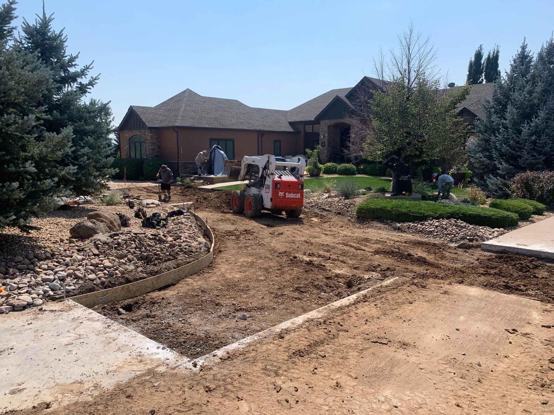 Bobcat moving dirt in front yard of a house during landscaping project; sunny day.