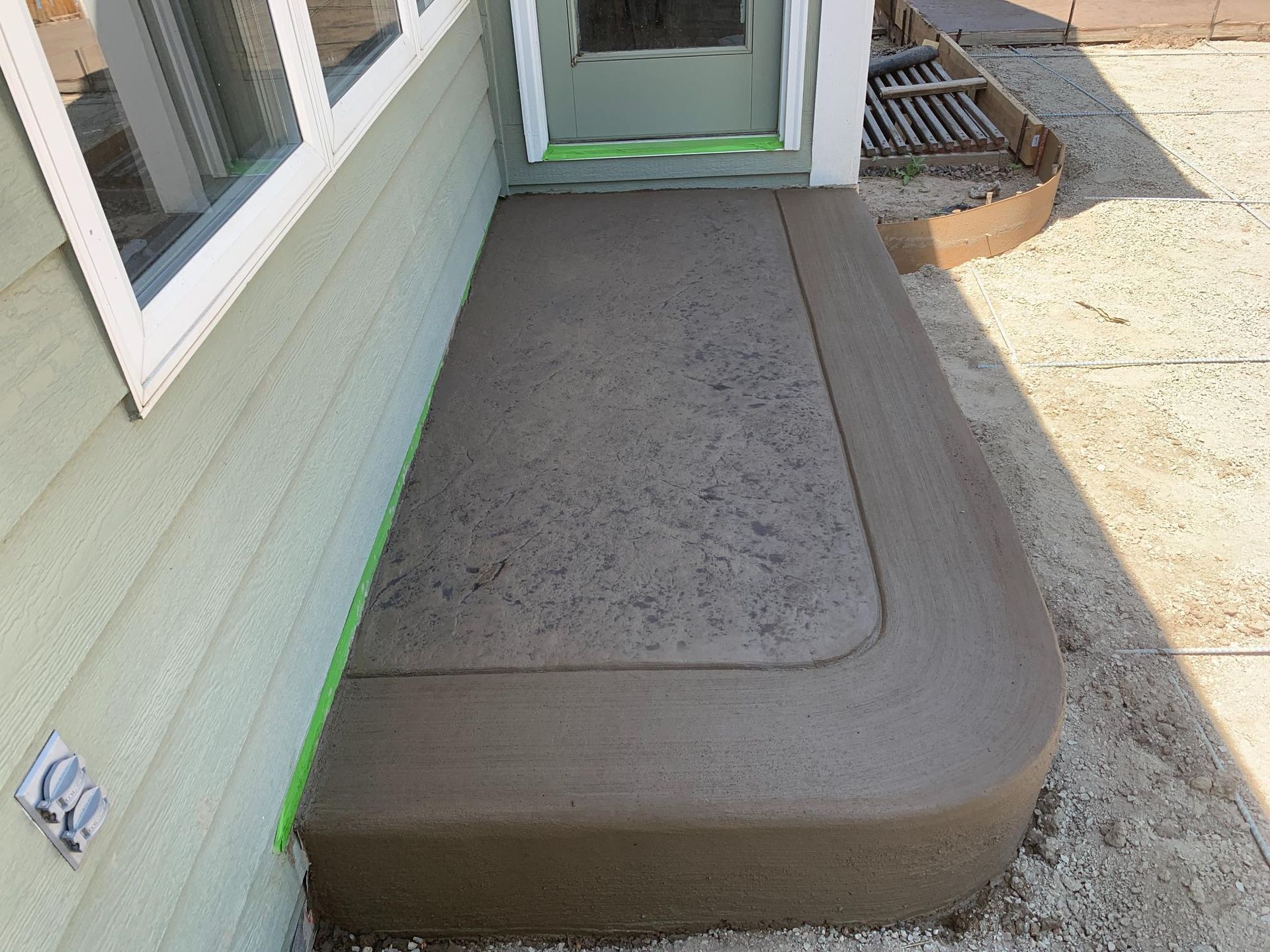 Freshly poured concrete stoop outside a house, with rounded corner and green tape along the wall.