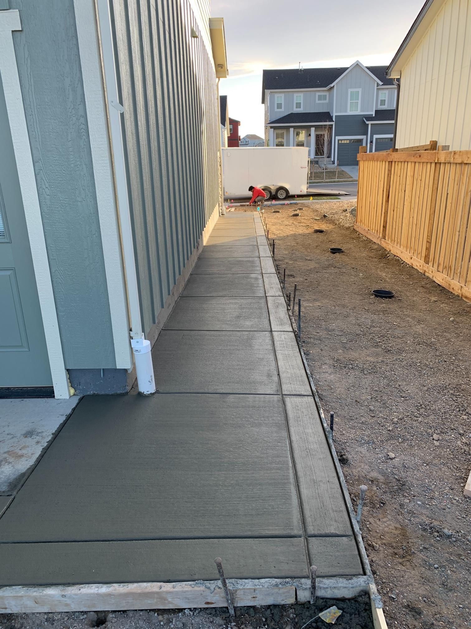 New concrete sidewalk next to a building, leading toward a residential area.