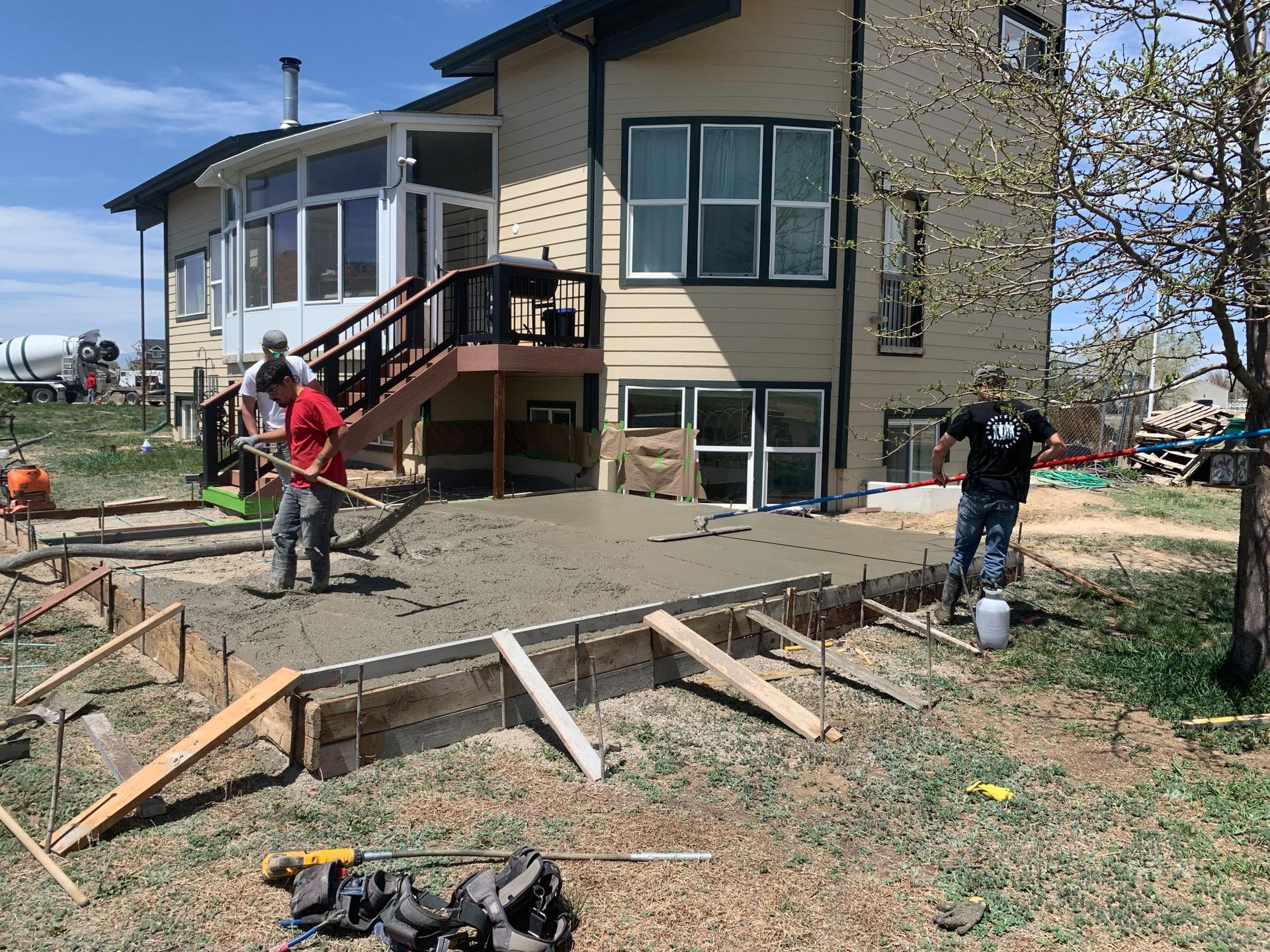 Construction workers leveling concrete on a patio outside a beige house.