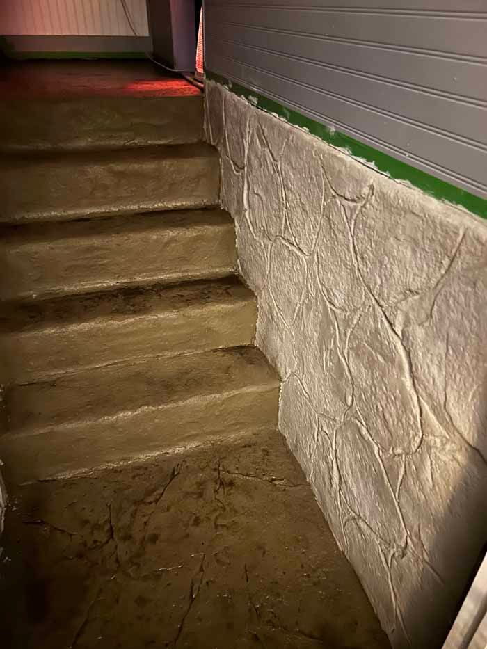 Concrete stairs leading up, beside a textured stone wall, green tape along the wall's edge.